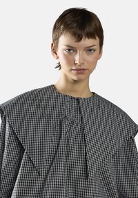 Sorte og hvide ternede oversized skjorte med en karakteristisk spids krave, der har sammensamlet stofdetaljer for tekstur og form.