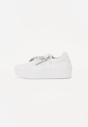 White platform sneakers with a textured sole, featuring a decorative chain and zipper detail on the side. Smooth leather material.