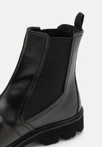 Bottes Chelsea en cuir noir avec panneaux élastiques côtelés, une languette de traction et une semelle épaisse en caoutchouc avec une bande de roulement texturée.