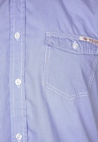 Blue striped button-up shirt made of fabric with a smooth texture. Features a patch pocket and white buttons with contrasting stitching.