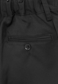 Czarne spodnie z tkaniny mają płaską kieszeń z poziomym otworem, ozdobioną okrągłym czarnym guzikiem na kieszeni.