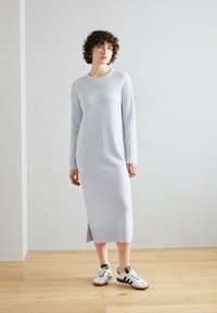 Lys grå strikket kjole med ribbede langermede og sidespalter. Laget av mykt materiale, har rund hals og en slim fit-design.