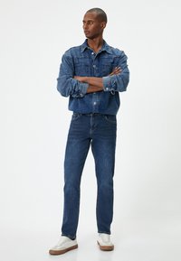 Denim-takkita ja farkut erinevates sinise tooni variantides, nupuga disain ja kaks rinna taskut. Valged jooksujalatsid täiendavad välimust.