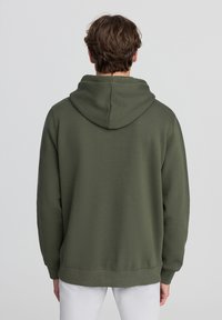 Felpa verde oliva con un ampio cappuccio, polsini e orlo a coste. Realizzata in un tessuto morbido con una vestibilità comoda, vista da dietro.