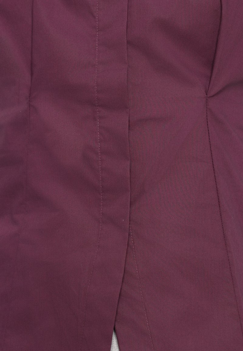 Bordeaux stof met een gladde textuur, voorzien van verticale naden en een lichte glans. Inclusief een zijsplit voor gemakkelijke beweging.