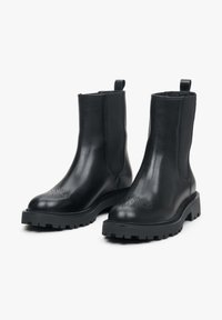 Czarne skórzane botki za kostkę o gładkiej fakturze, z elastycznymi bocznymi panelami i trwałą podeszwą przegubową. Posiadają dekoracyjne perforacje na palcach.