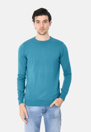 Maglione azzurro a collo rotondo realizzato in tessuto liscio, con maniche lunghe e polsini a coste. Abbinato a jeans azzurri chiari.