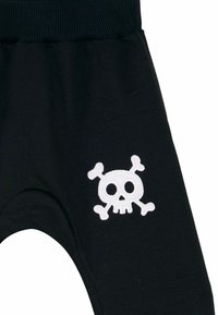 Jogger neri con vita a coste, caratterizzati da un design ricamato di teschio e due tibie bianche sulla parte bassa della gamba. Materiale morbido, vestibilità rilassata.