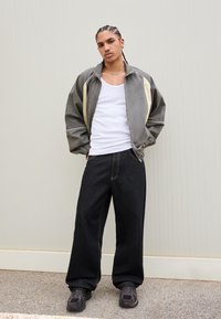 Grå og creme vindjakke med høj krave, parret med løse sorte jeans og mørke sneakers. Glat stof med kontrasterende accenter.