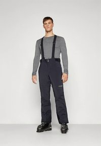 Črne smučarske hlače z nastavljivimi naramnicami, z gumbnim zapiranjem in izoliranim materialom. Oblečene s sivo majico z dolgimi rokavi in črnimi smučarskimi čevlji.