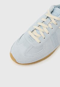 Baskets en daim bleu clair avec lacets crème et semelle en gomme, présentant des coutures détaillées et une languette rembourrée.