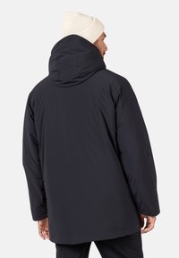 Abrigo acolchado negro con una gran capucha, con una textura suave y un ajuste relajado, visto desde la parte de atrás. Gorro de lana blanco visible.