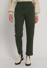 Gröna cargobyxor med sidofickor, rak bendesign, tillverkade i bomull och med en mjuk yta. Bärs med en krämfärgad tröja och beige stövlar.