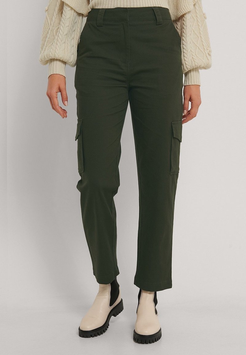 Groene cargobroek met zijzakken, rechte pijpdesign, van katoen en met een gladde textuur. G gedragen met een crème trui en beige laarzen.