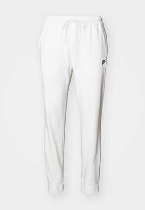 Hvite joggebukser laget av mykt stoff, med snøring i livet, smalere ben og en liten svart logo på venstre side.