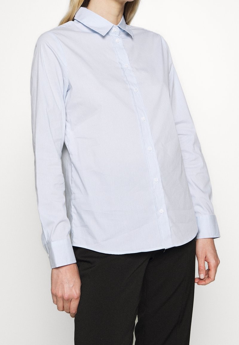 Camicia azzurra chiaro con righe bianche, maniche lunghe e colletto standard. Il tessuto appare liscio con una vestibilità su misura.