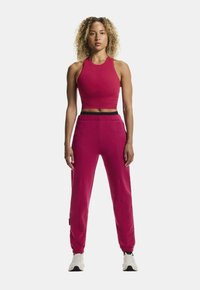 Tætsiddende lyserød crop top og matchende tapered joggers lavet af blødt stof. Har et sort elastisk taljebånd og ankels elastikker for ekstra komfort.