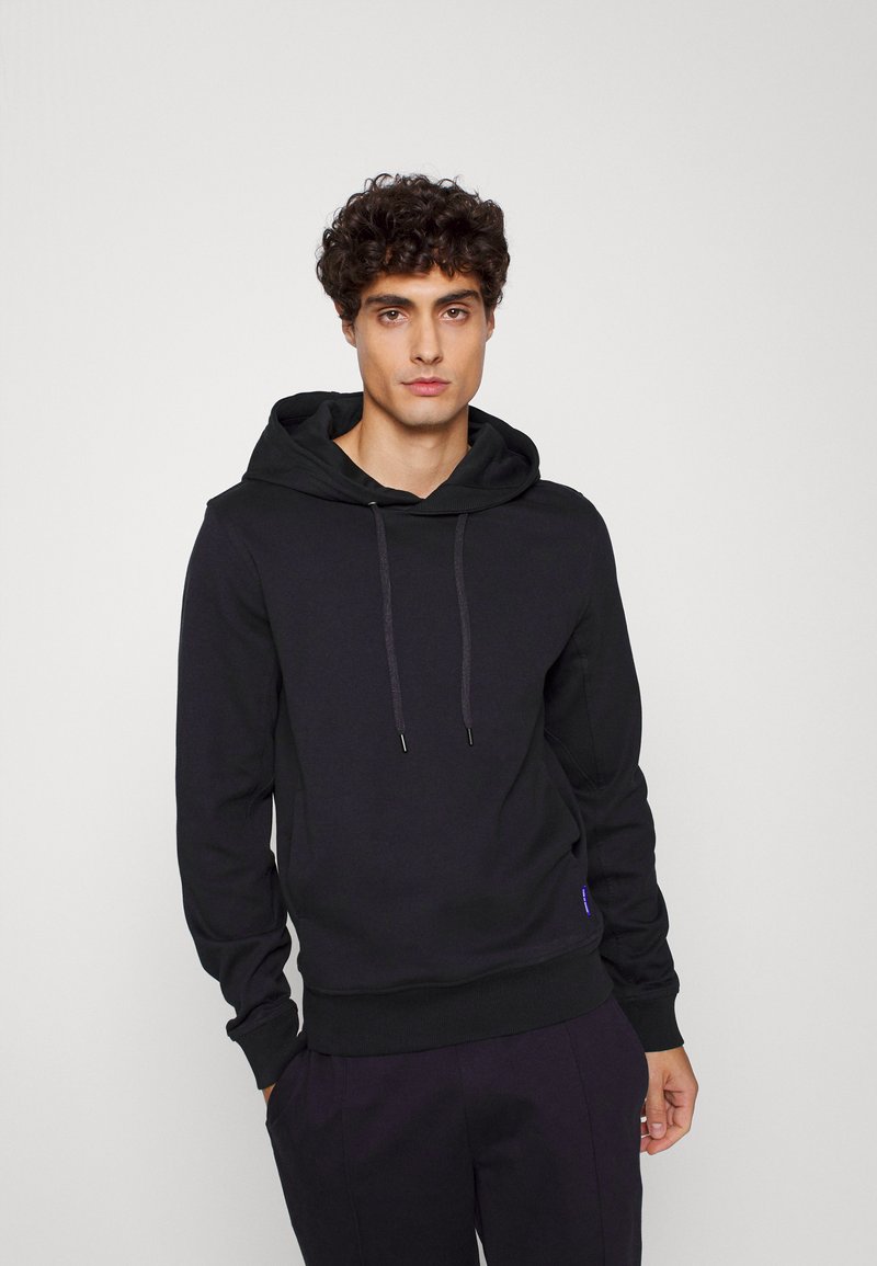 Sweatshirt preto com capuz em material suave, apresentando cordões, punhos canelados, e uma pequena etiqueta de logotipo na parte inferior. Design minimalista.