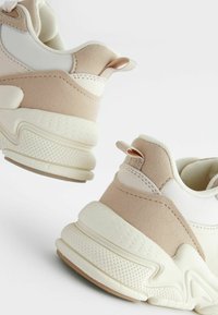 Baskets chunky avec une combinaison de matériaux beiges et blancs, des accents texturés, une pointe ronde et une languette au talon.