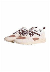 Sneaker beige chiaro con dettagli marroni, materiali in suede e mesh, lacci a fantasia e una spessa suola bianca, dotati di un collare imbottito.