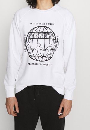 Chemise blanche à manches longues avec un graphique de globe noir montrant des figures humaines liées et le texte "L'avenir est radieux, ensemble nous réussissons."