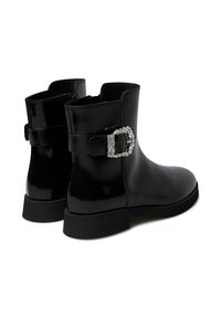 Stivaletti in vernice nera alla caviglia con una fibbia decorativa impreziosita da strass trasparenti, texture liscia e suola in gomma bassa.