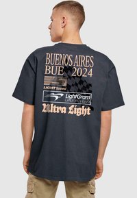 Cămașă neagră din bumbac, cu un design grafic pe spate ce conține textul "BUENOS AIRES BUE 2024" în nuanță de bej, alături de mai multe logo-uri și un model căptușit.