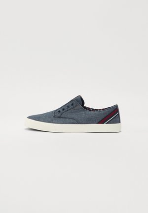 Navy canvas instappers met een lichte zool. Kenmerken zijn een getextureerde bovenkant, ronde neus en gestreepte accent op de hiel. Geruit voering zichtbaar aan de binnenkant.