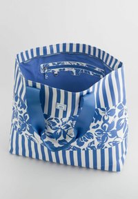 Niebieska i biała torba na ramię z kwiatowymi i paskowanymi wzorami, z zamykaną na zamek kieszenią wewnętrzną i niebieskimi uchwytami. Wykonana z trwałego materiału.