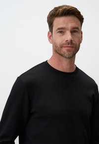 Felpa nera in cotone con colletto rotondo, maniche lunghe e texture liscia. Presenta dettagli sottili sulle spalle e una silhouette aderente.
