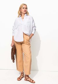 Chemise blanche à manches longues, pantalon large beige clair, sandales à lanières marron et sac à main en franges marron. Design simple et texture douce.