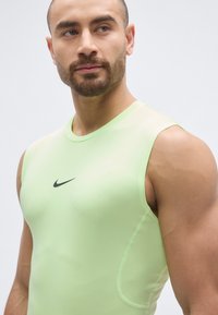 Sport tank top in light green, made from stretchy fabric. Features a round neckline, sleeveless design, and black Nike logo on the chest.