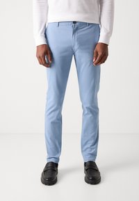 Helle blaue Baumwollhose im Slim-Fit, mit einem Knopfverschluss und Taschen, kombiniert mit schwarzen Schuhen. Glatte Textur und minimalistisches Design.