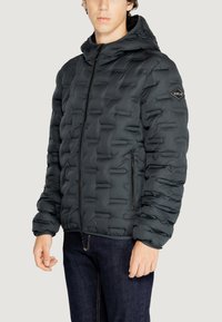 Giubbotto piumino nero con design trapuntato, frontale con zip e cappuccio. Caratteristiche includono tasche laterali e un accento con logo sulla spalla.