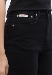 Μαύρο τζιν με στενή εφαρμογή, με ετικέτα Calvin Klein στην μπροστινή τσέπη και αξεσουάρ σε ασημί απόχρωση.