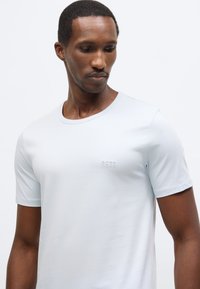 Svetlo modra majica s kratkimi rokavi iz gladkega blaga, z okroglim izrezom in subtilno reliefno napisom "BOSS" na prsih.