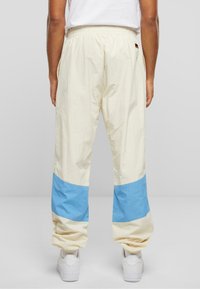 Pantaloni crem ușori cu un panou inferior albastru, talie elastică și gleznă cu tiv, asortați cu adidași albi. Țesătură texturată.