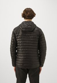 Sort pufjakke med horisontale syninger, hætte og en glat, blank overflade. Har slim fit og elastiske manchetter.