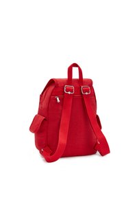 Mochila de tela roja con correas ajustables, asa superior, bolsillo lateral y herrajes plateados. Incluye un compartimento principal con cremallera.