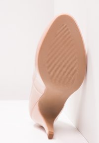 Naken högklackad sko med spetsig tå, glansig yta och texturerad gummisula. Klacken är tunn och kurvig för en elegant profil.