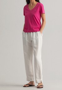 Różowa koszulka z krótkim rękawem i dekoltem w serek, zestawiona z białymi, lekkimi spodniami, charakteryzującymi się luźnym krojem i casualowym stylem. Czarne klapki dopełniają outfit.