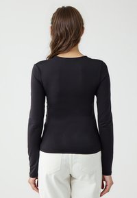 Chemise à manches longues noire avec une coupe ajustée, col rond, texture lisse, affichant un style simple sans motifs ni accents visibles.