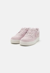 Sneaker in suede rosa chiaro con suola in gomma bianca, design con lacci, punta perforata e logo Swoosh rosa lucido di lato.