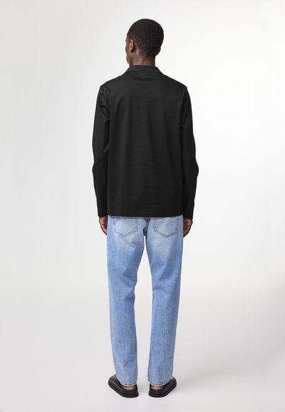 Zwarte longsleeve shirt met een rechte snit, gecombineerd met lichtblauwe straight-leg jeans en zwarte instappers. Minimalistisch ontwerp.