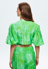 Groene cropped top met pofmouwen, met een bloemenpatroon. Het materiaal lijkt lichtgewicht, met een licht gestructureerde afwerking.