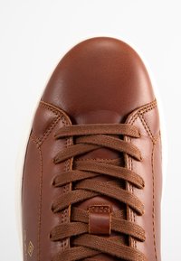 Braune Leder-Sneaker mit runder Zehenpartie, strukturiertem Oberfläche, weißer Gummisohle und braunen Schnürsenkeln. Verfügt über genähte Akzente und Logo-Details.