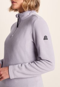 Light purple fleece pullover with a half-zip collar, long sleeves, and a logo patch on the left arm. Soft texture with a comfortable fit.