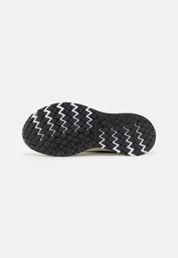 Semelle de chaussure noire avec des lignes blanches en zigzag et un motif de bande de roulement triangulaire texturé sur un fond clair uni.