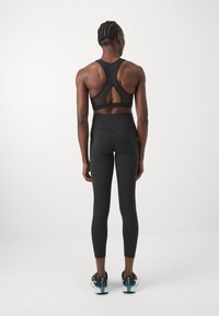 Czarny sportowy biustonosz z wycięciem typu racerback i panelem z siateczki. Zestawiony z wysokim stanem czarnych legginsów oraz butami sportowymi z turkusowymi akcentami.