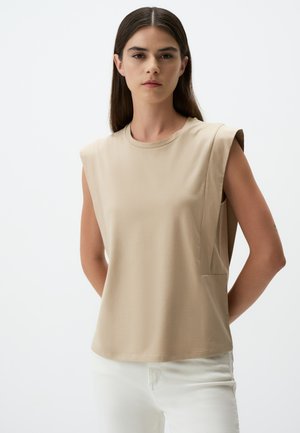 Haut beige sans manches avec un col rond, texture lisse, poche latérale et design structuré des épaules. Le tissu semble léger.